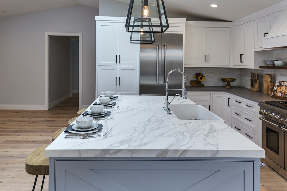 Example of a classic eat-in kitchen design in Orange County with an integrated sink, white cabinets, solid surface countertops, white backsplash, stone slab backsplash and an island