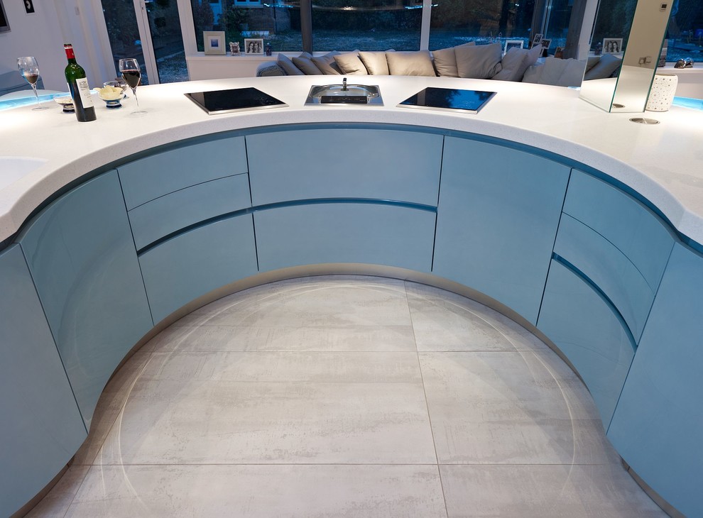 Photo of an expansive modern u-shaped kitchen/diner in London with an integrated sink, flat-panel cabinets, blue cabinets, composite countertops, blue splashback, glass sheet splashback, stainless steel appliances, marble flooring and an island.