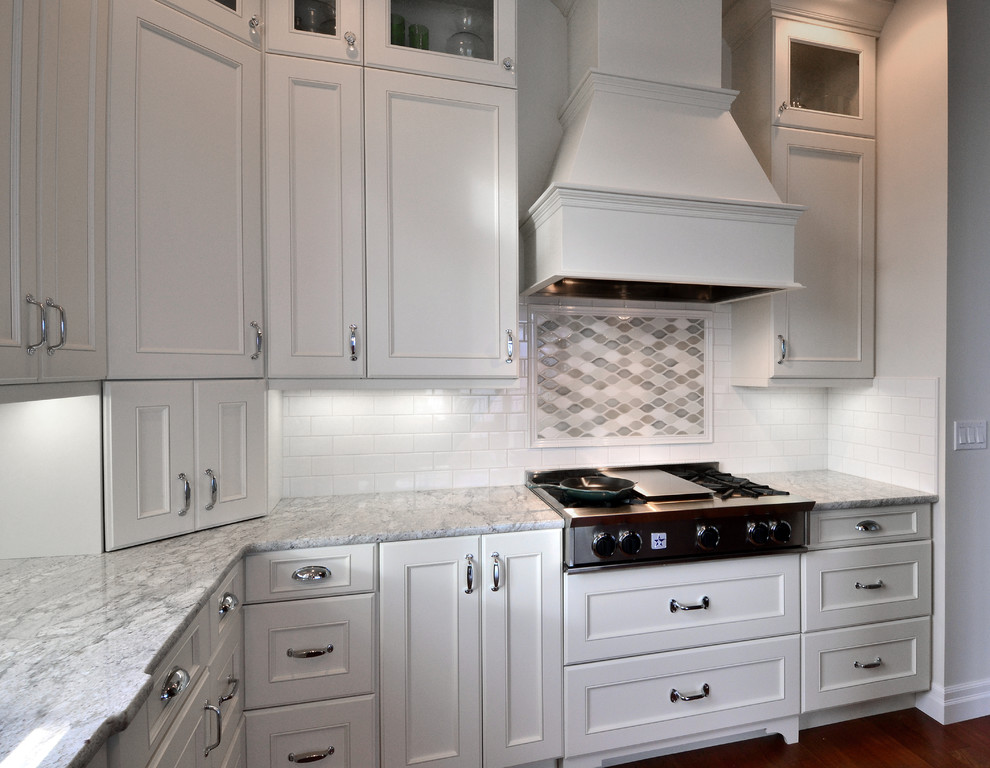 Cette photo montre une cuisine avec des portes de placard blanches, plan de travail en marbre, une crédence blanche, une crédence en carrelage métro, un électroménager en acier inoxydable et un sol en bois brun.