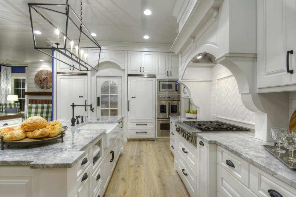 Design ideas for an expansive traditional l-shaped kitchen/diner in Denver with raised-panel cabinets, white cabinets, granite worktops, white splashback, stainless steel appliances, light hardwood flooring and multiple islands.
