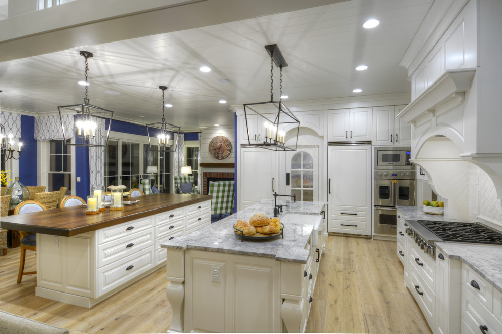Expansive traditional l-shaped kitchen/diner in Denver with raised-panel cabinets, white cabinets, granite worktops, white splashback, stainless steel appliances, light hardwood flooring and multiple islands.
