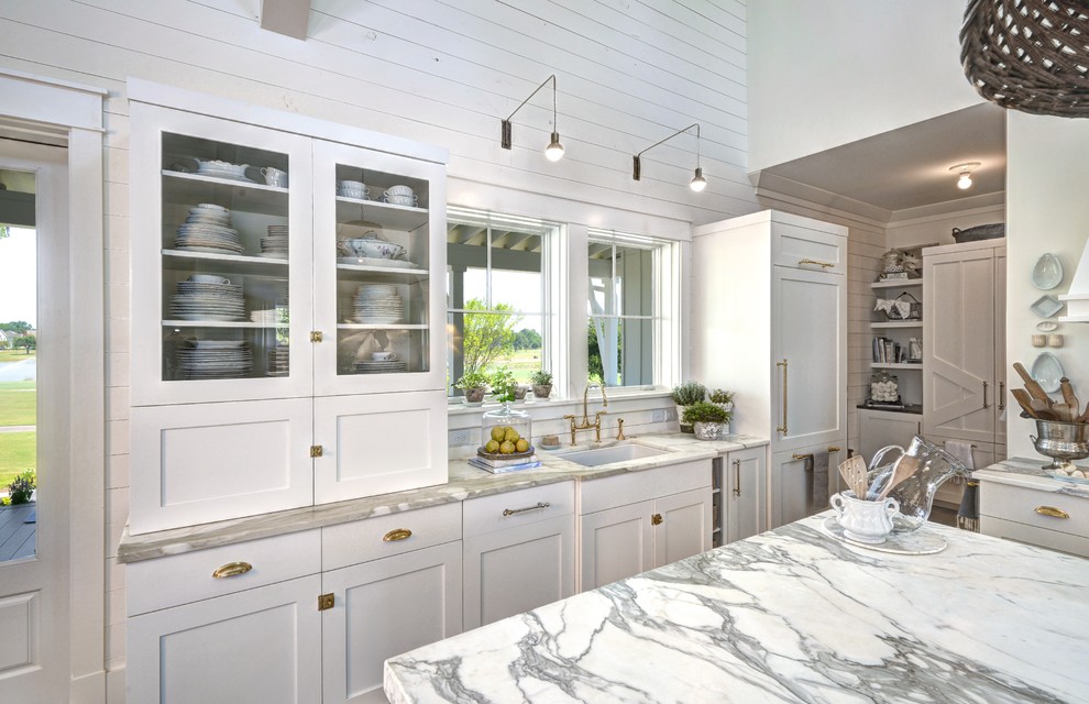 Photo of a large farmhouse l-shaped kitchen/diner in Charleston with white cabinets, marble worktops, white appliances, an island, a submerged sink, shaker cabinets, grey splashback, stone slab splashback and light hardwood flooring.