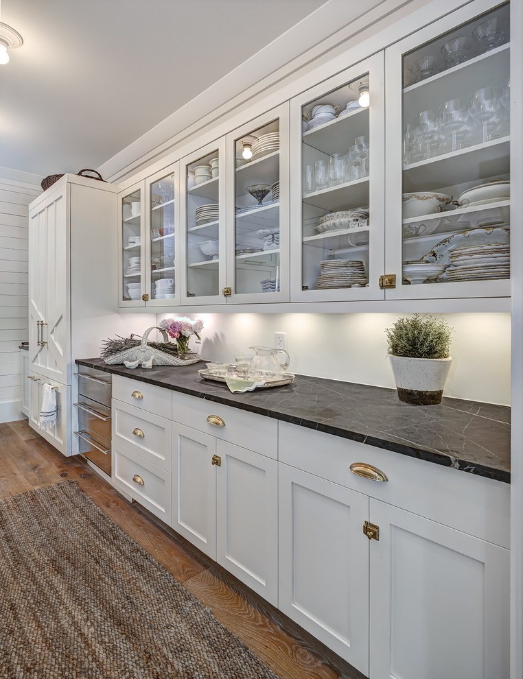 Exemple d'une grande cuisine américaine encastrable et linéaire nature avec une crédence blanche, des portes de placard blanches, plan de travail en marbre, îlot, un placard à porte shaker et un sol en bois brun.
