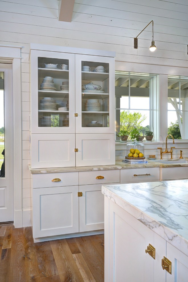 Inredning av ett lantligt stort kök, med vita skåp, marmorbänkskiva, vita vitvaror, en köksö, en undermonterad diskho, skåp i shakerstil, grått stänkskydd, stänkskydd i sten och ljust trägolv