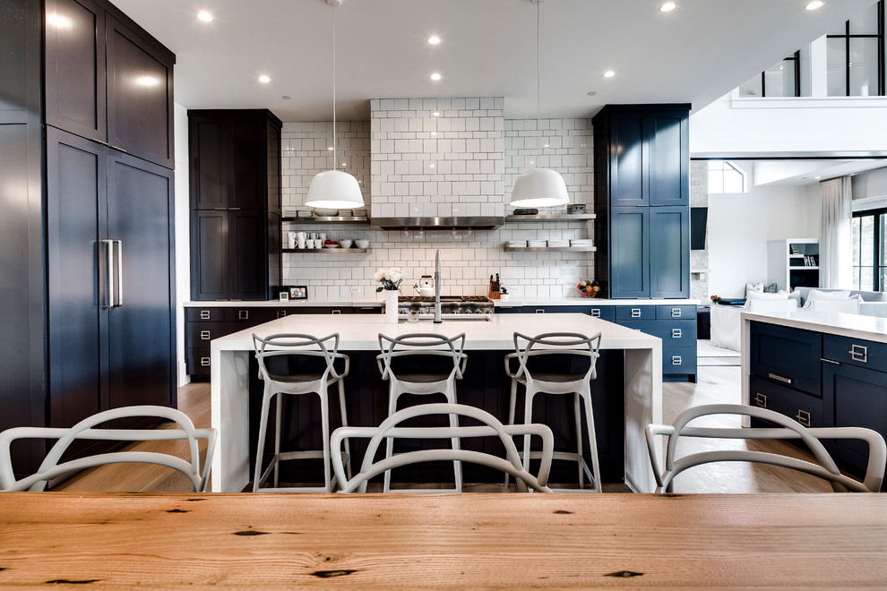 Classic u-shaped kitchen/diner in DC Metro with a submerged sink, shaker cabinets, blue cabinets, white splashback, integrated appliances, medium hardwood flooring, an island, brown floors and white worktops.