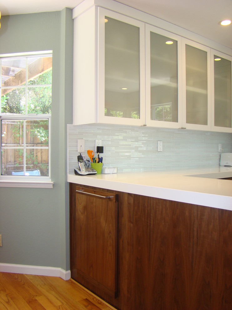 Bild på ett minimalistiskt vit vitt l-kök, med en undermonterad diskho, släta luckor, skåp i mörkt trä, bänkskiva i koppar, blått stänkskydd, stänkskydd i glaskakel och rostfria vitvaror