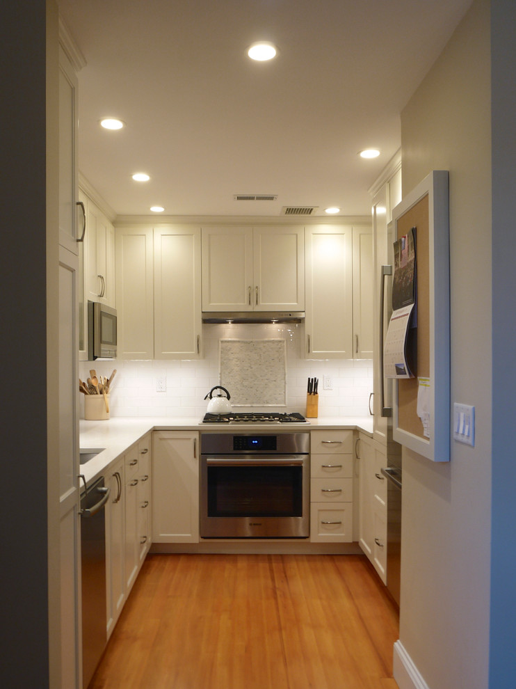 Example of a small transitional u-shaped light wood floor kitchen design in Boston with an undermount sink, shaker cabinets, white cabinets, quartz countertops, white backsplash, stone tile backsplash, stainless steel appliances and no island