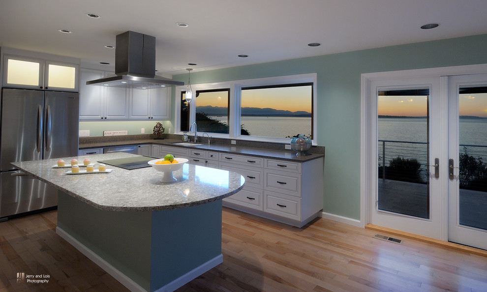 Bild på ett stort maritimt kök, med en undermonterad diskho, luckor med upphöjd panel, vita skåp, bänkskiva i kvartsit, grönt stänkskydd, rostfria vitvaror, ljust trägolv och en köksö