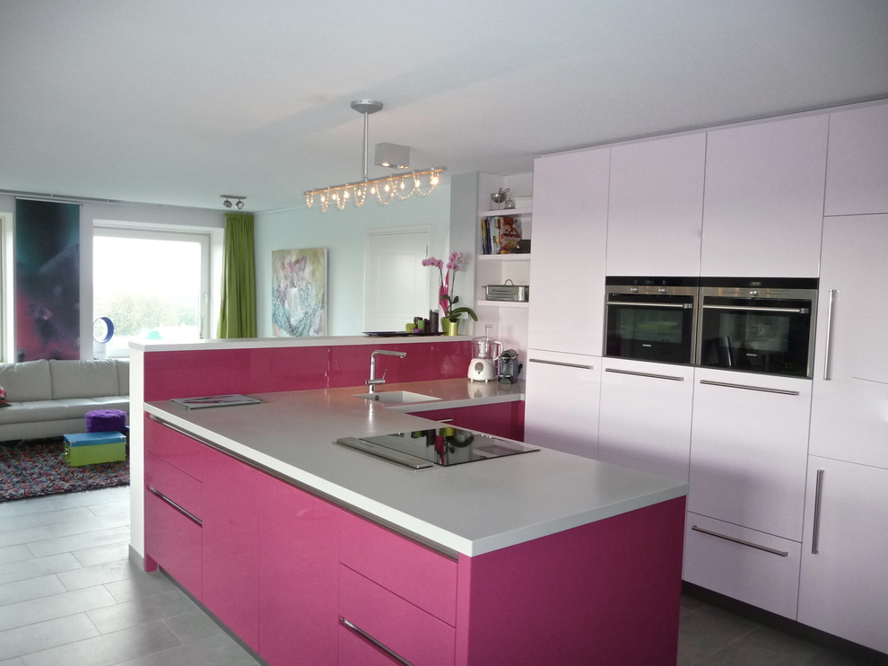 Immagine di una cucina minimalista di medie dimensioni con lavello sottopiano, ante lisce, ante rosse, top in quarzite, paraspruzzi rosa, elettrodomestici da incasso, pavimento con piastrelle in ceramica e penisola
