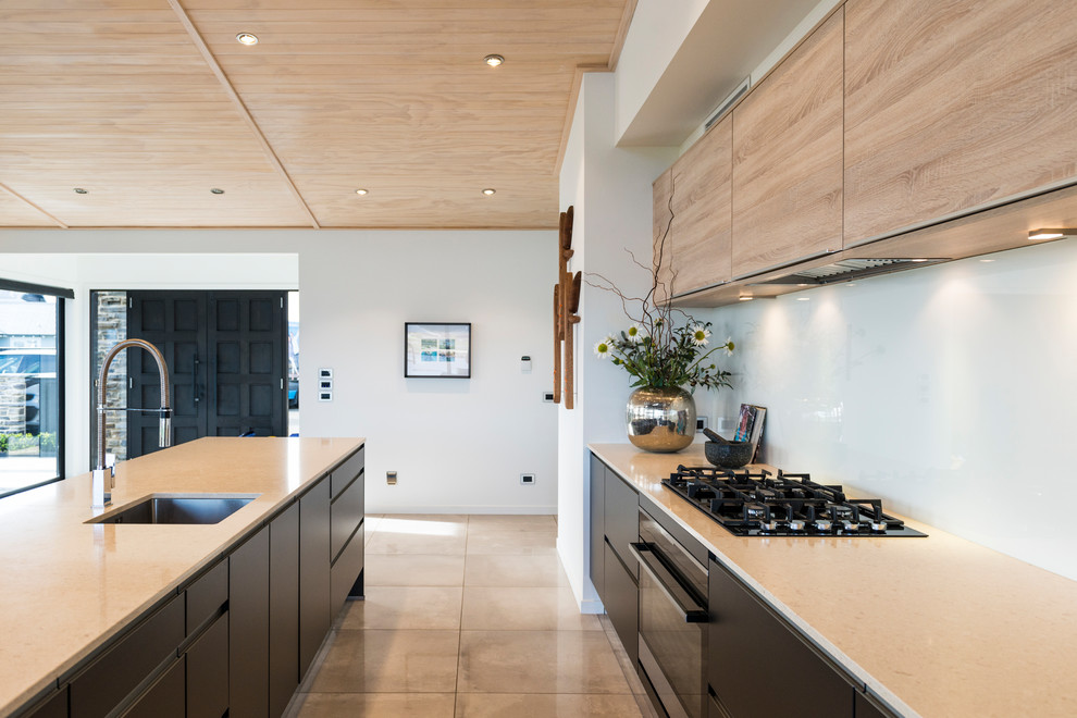 Inspiration for a large contemporary galley kitchen pantry remodel in Auckland with an undermount sink, flat-panel cabinets, light wood cabinets, quartz countertops, white backsplash, glass sheet backsplash, black appliances and an island
