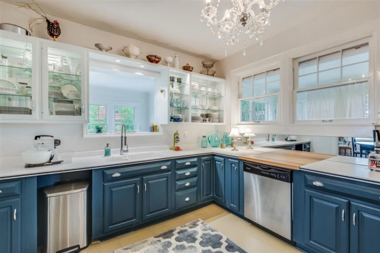 Example of a mid-sized transitional u-shaped painted wood floor and gray floor enclosed kitchen design in Other with an integrated sink, open cabinets, blue cabinets, solid surface countertops, white backsplash, mirror backsplash and stainless steel appliances