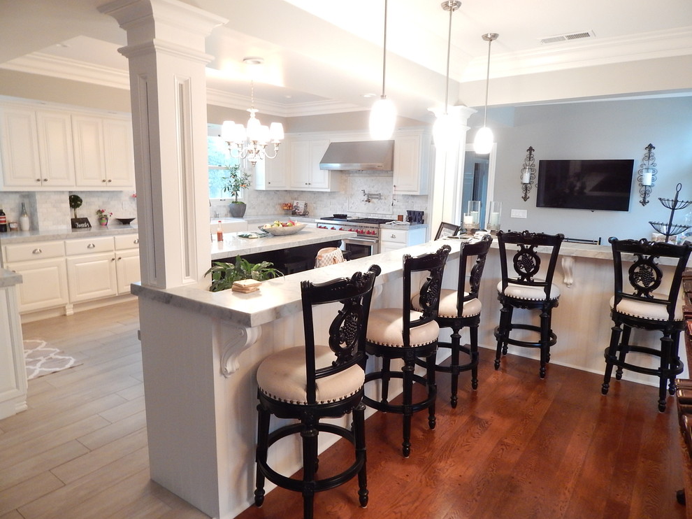 Example of a mid-sized trendy u-shaped dark wood floor open concept kitchen design in Sacramento with a farmhouse sink, raised-panel cabinets, white cabinets, soapstone countertops, gray backsplash, stone tile backsplash, stainless steel appliances and an island