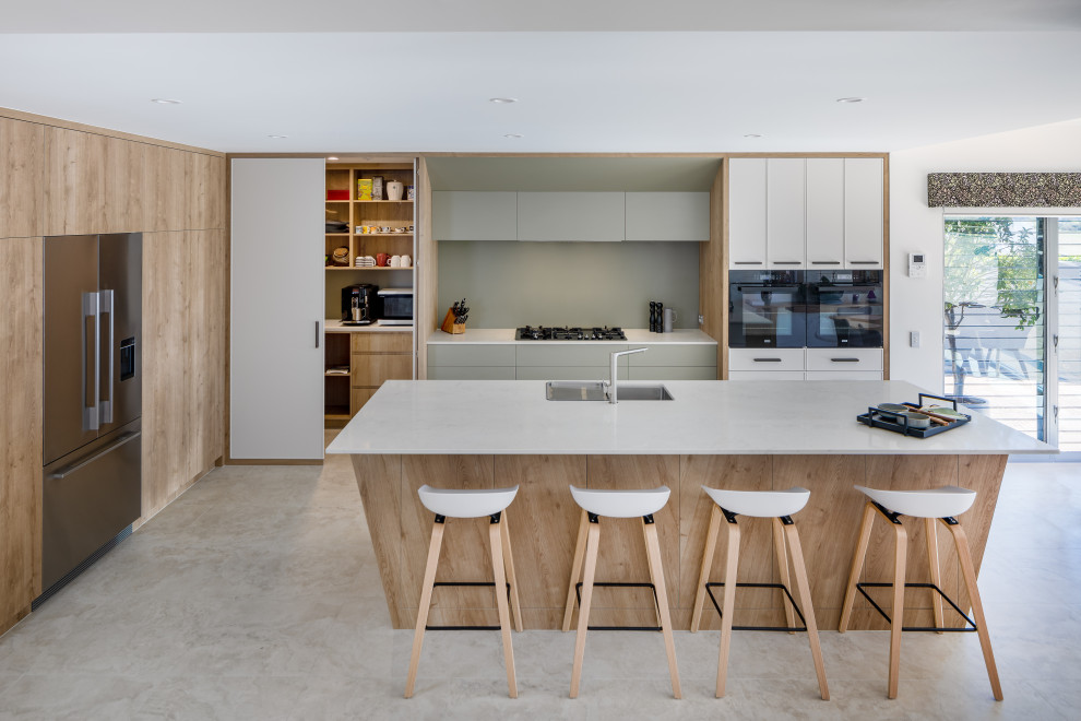 Large contemporary l-shaped kitchen in Perth with a double-bowl sink, engineered stone countertops, green splashback, glass sheet splashback, black appliances, porcelain flooring, an island, flat-panel cabinets, white cabinets, grey floors and white worktops.