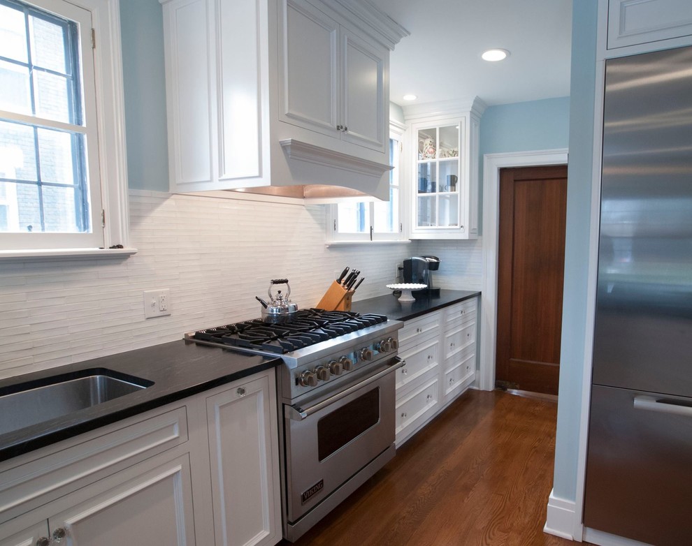 This is an example of a large traditional kitchen/diner in New York with glass-front cabinets, white cabinets, white splashback, stainless steel appliances and medium hardwood flooring.