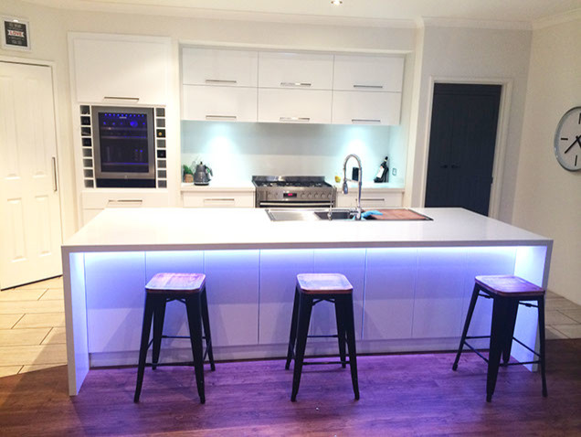 Small modern single-wall kitchen/diner in Perth with a submerged sink, flat-panel cabinets, white cabinets, engineered stone countertops, white splashback, glass sheet splashback, stainless steel appliances, light hardwood flooring and an island.