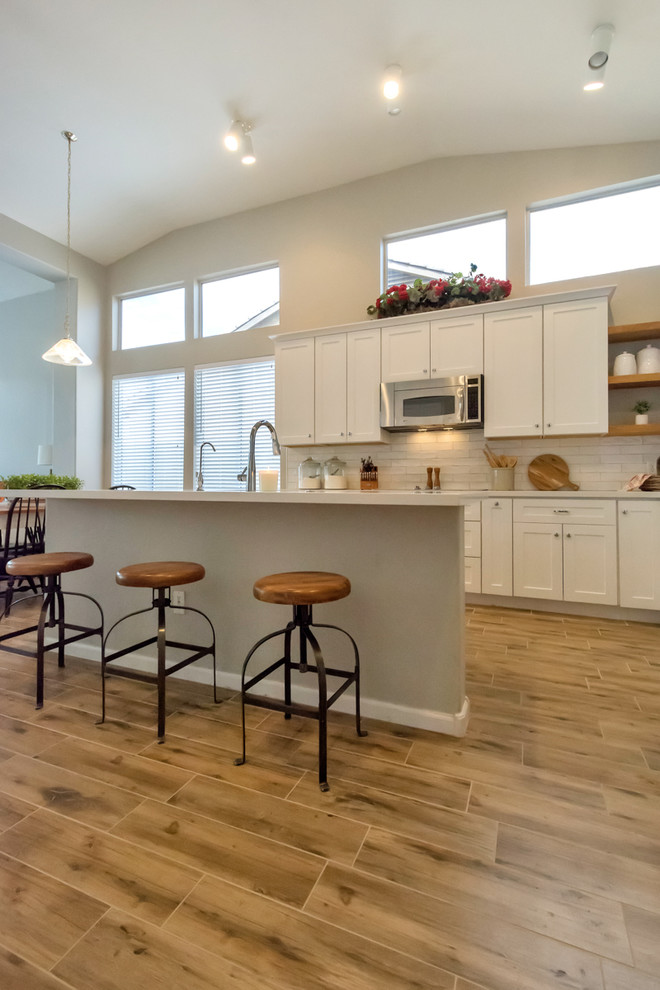 Inspiration for a large country l-shaped porcelain tile and brown floor eat-in kitchen remodel in Phoenix with a farmhouse sink, shaker cabinets, white cabinets, quartzite countertops, white backsplash, subway tile backsplash, stainless steel appliances and an island