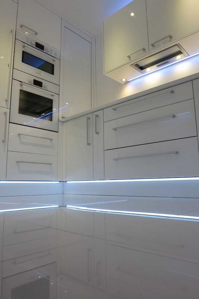 Inspiration for a small modern u-shaped enclosed kitchen in Hampshire with a submerged sink, flat-panel cabinets, white cabinets, white splashback, glass sheet splashback, white appliances, ceramic flooring and no island.