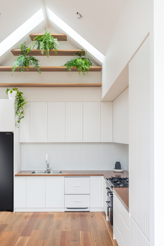 メルボルンにある高級な小さな北欧スタイルのおしゃれなキッチン (ダブルシンク、フラットパネル扉のキャビネット、白いキャビネット、木材カウンター、白いキッチンパネル、メタルタイルのキッチンパネル、黒い調理設備、無垢フローリング、アイランドなし、茶色い床、茶色いキッチンカウンター、三角天井) の写真