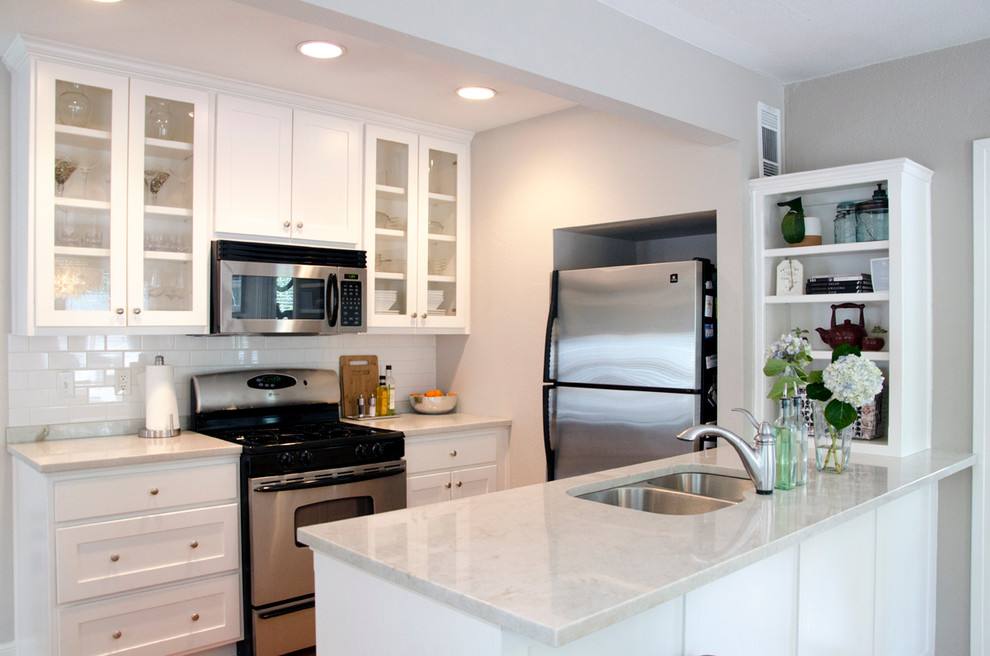 オースティンにあるトランジショナルスタイルのおしゃれなキッチン (ダブルシンク、ガラス扉のキャビネット、白いキッチンパネル、サブウェイタイルのキッチンパネル、シルバーの調理設備) の写真