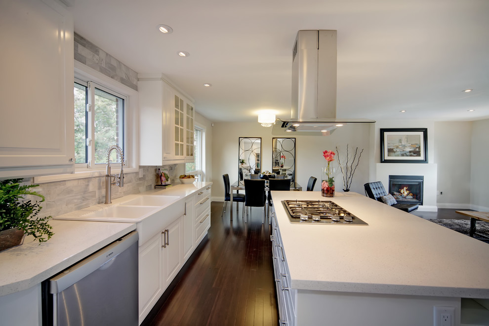 This is an example of a medium sized modern l-shaped open plan kitchen in Toronto with raised-panel cabinets, white cabinets, stainless steel appliances, dark hardwood flooring, an island, a belfast sink, engineered stone countertops, grey splashback, stone tiled splashback and brown floors.