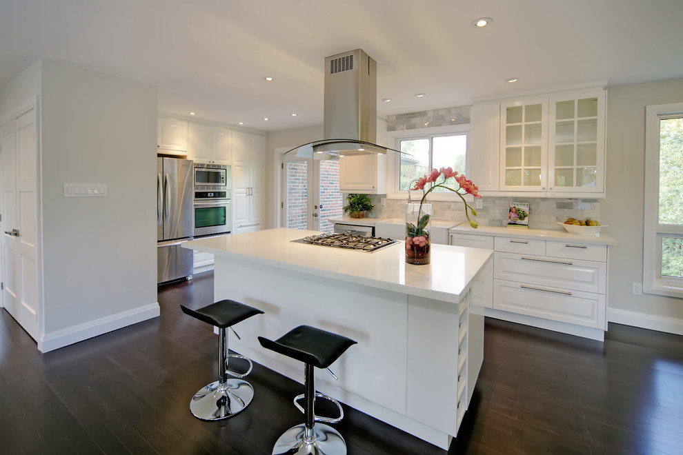Mid-sized minimalist l-shaped dark wood floor and brown floor open concept kitchen photo in Toronto with a farmhouse sink, raised-panel cabinets, white cabinets, quartz countertops, gray backsplash, stone tile backsplash, stainless steel appliances and an island