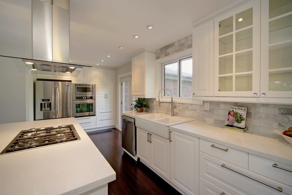 Modern inredning av ett mellanstort kök, med en rustik diskho, luckor med upphöjd panel, vita skåp, bänkskiva i kvarts, grått stänkskydd, stänkskydd i stenkakel, rostfria vitvaror, mörkt trägolv och en köksö
