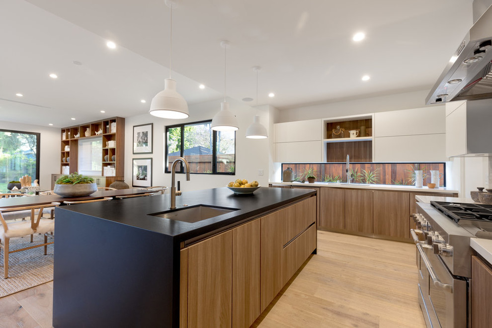 Inspiration for a contemporary l-shaped kitchen in Los Angeles with a submerged sink, flat-panel cabinets, medium wood cabinets, window splashback, stainless steel appliances, medium hardwood flooring, an island, brown floors and black worktops.