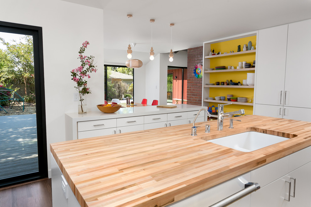 Example of a mid-sized 1960s u-shaped medium tone wood floor and brown floor eat-in kitchen design in Los Angeles with a double-bowl sink, flat-panel cabinets, white cabinets, wood countertops, yellow backsplash, ceramic backsplash, stainless steel appliances and an island