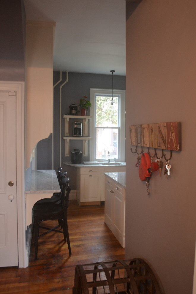 Immagine di un piccolo cucina con isola centrale vittoriano con ante con bugna sagomata, ante bianche, top in marmo e pavimento in legno massello medio