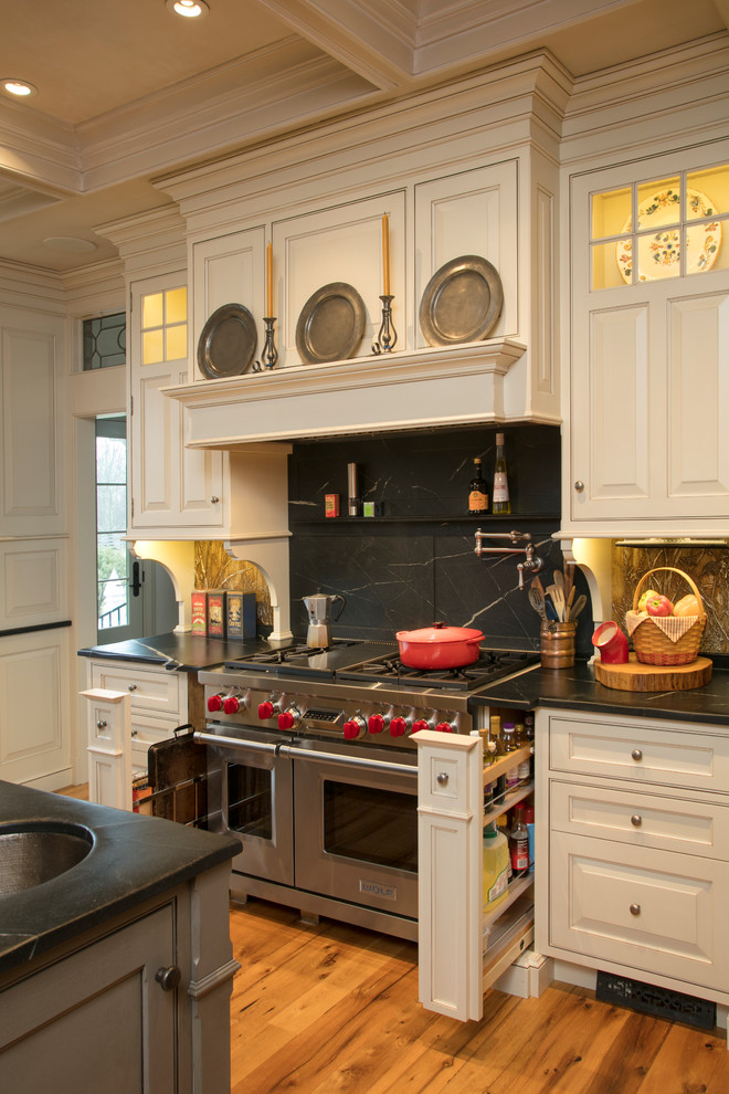 Exempel på ett stort lantligt kök, med en integrerad diskho, luckor med profilerade fronter, vita skåp, bänkskiva i täljsten, svart stänkskydd, stänkskydd i sten, integrerade vitvaror, mellanmörkt trägolv och en köksö