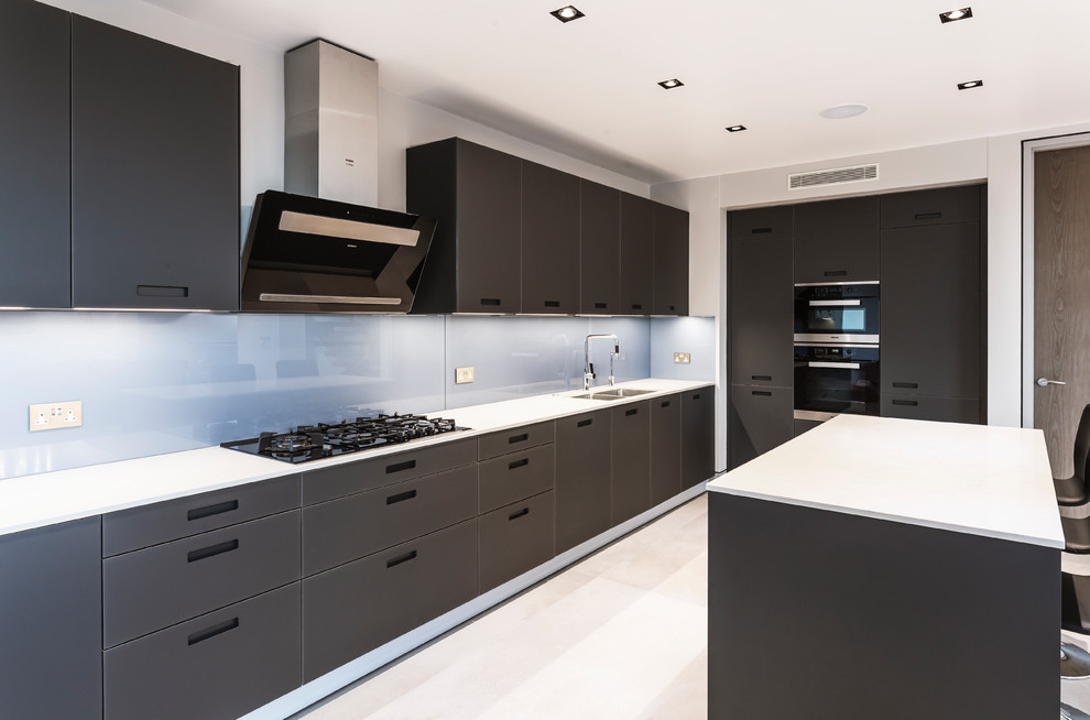 Example of a trendy beige floor kitchen design in London with a double-bowl sink, flat-panel cabinets, gray cabinets, blue backsplash, glass sheet backsplash, black appliances, an island and white countertops