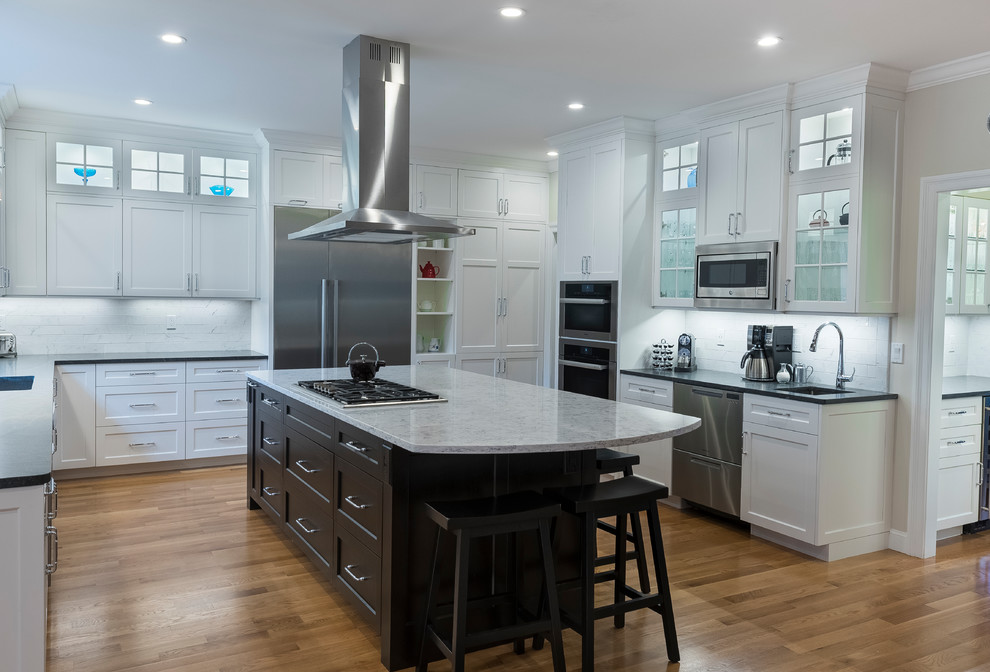 Inspiration for an expansive traditional kitchen pantry in Boston with a single-bowl sink, shaker cabinets, white cabinets, engineered stone countertops, white splashback, porcelain splashback, stainless steel appliances, medium hardwood flooring, an island and brown floors.