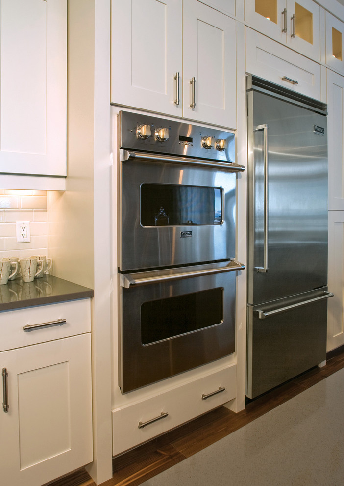 Cette photo montre une cuisine tendance avec un placard avec porte à panneau encastré, des portes de placard blanches et un électroménager en acier inoxydable.