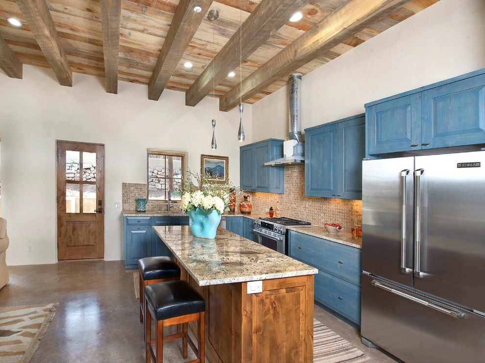 Example of a mountain style l-shaped concrete floor kitchen design in Albuquerque with an undermount sink, raised-panel cabinets, blue cabinets, granite countertops, beige backsplash, stone tile backsplash, stainless steel appliances and an island