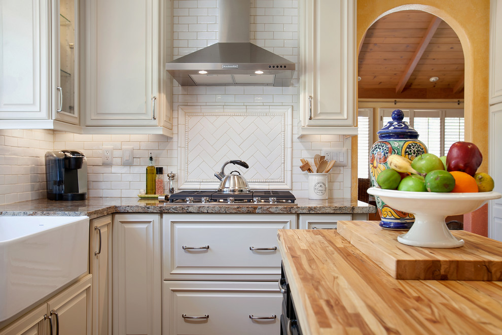 Bild på ett stort vintage kök, med en rustik diskho, luckor med upphöjd panel, vita skåp, granitbänkskiva, vitt stänkskydd, stänkskydd i tunnelbanekakel, rostfria vitvaror, mellanmörkt trägolv och en köksö