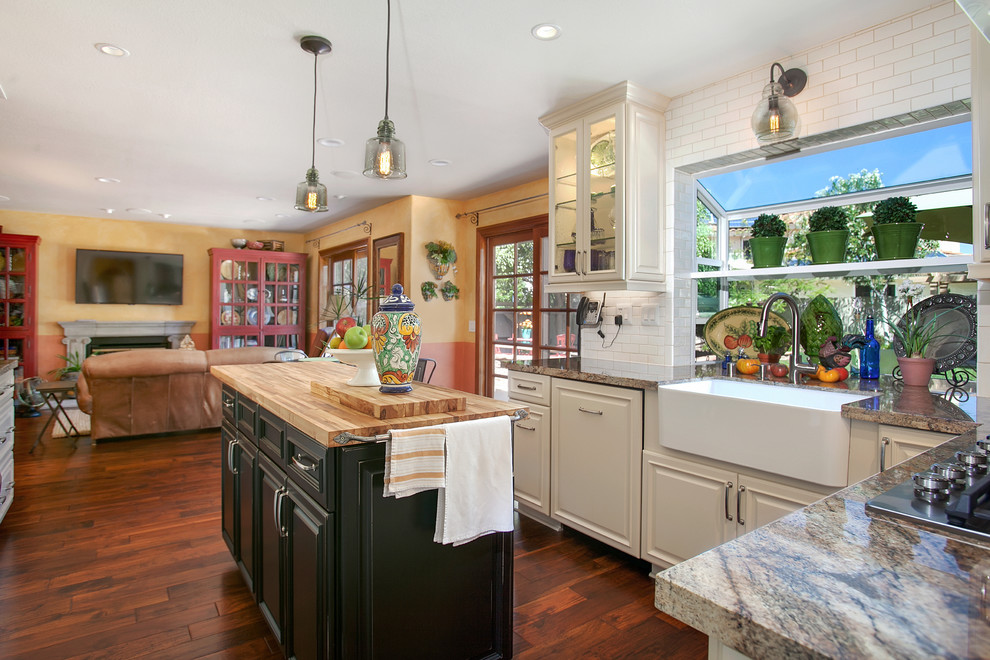 Large elegant u-shaped medium tone wood floor eat-in kitchen photo in San Diego with a farmhouse sink, raised-panel cabinets, white cabinets, granite countertops, white backsplash, subway tile backsplash, stainless steel appliances and an island