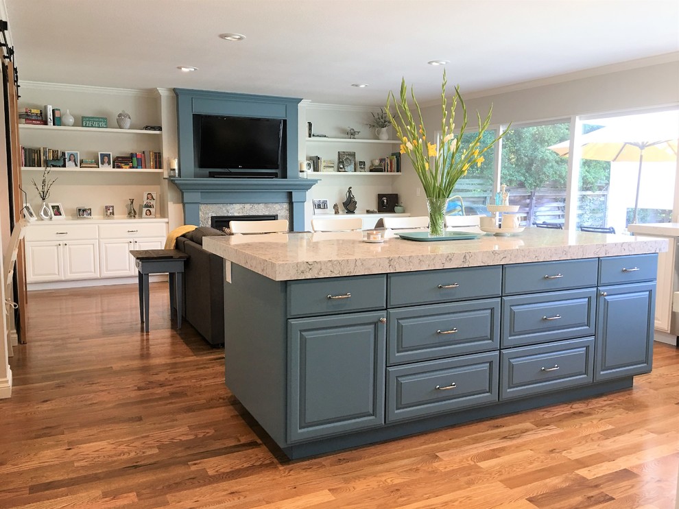 Example of a mid-sized cottage l-shaped medium tone wood floor and brown floor open concept kitchen design in San Francisco with a farmhouse sink, raised-panel cabinets, blue cabinets, quartz countertops, gray backsplash, glass tile backsplash, stainless steel appliances and an island