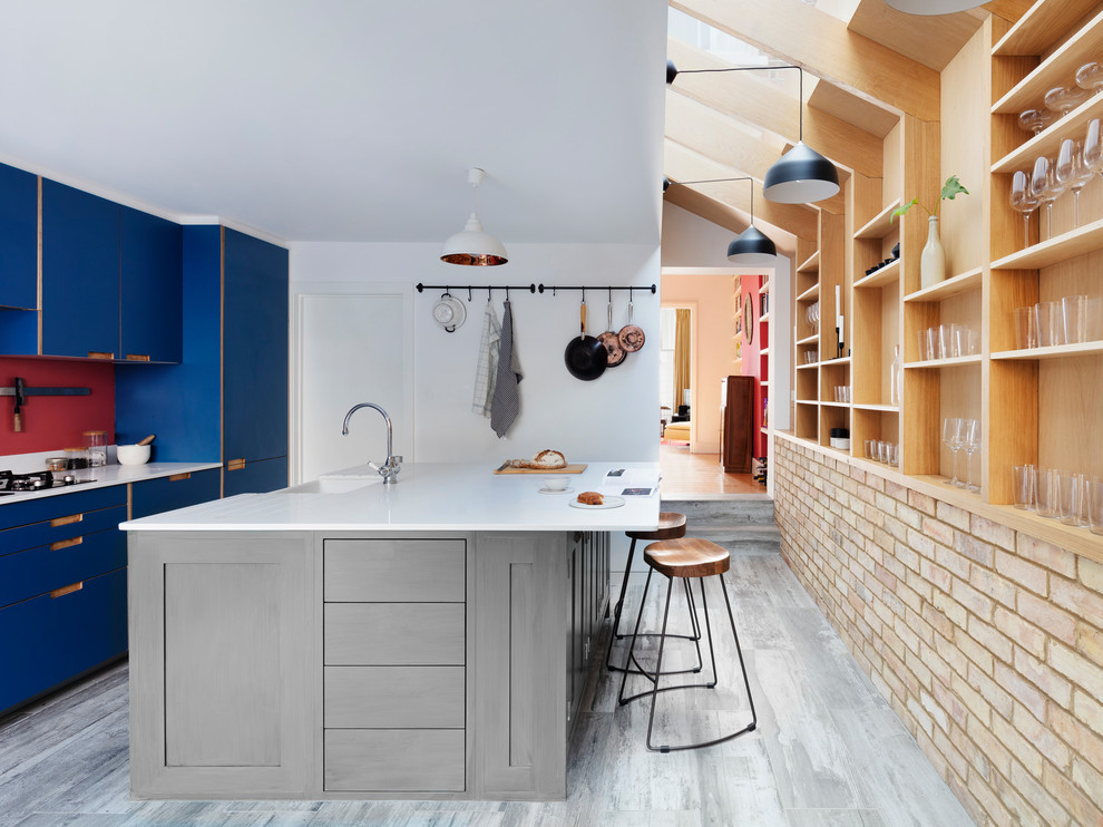 ロンドンにある北欧スタイルのおしゃれなキッチン (エプロンフロントシンク、フラットパネル扉のキャビネット、青いキャビネット、赤いキッチンパネル、グレーの床、白いキッチンカウンター) の写真