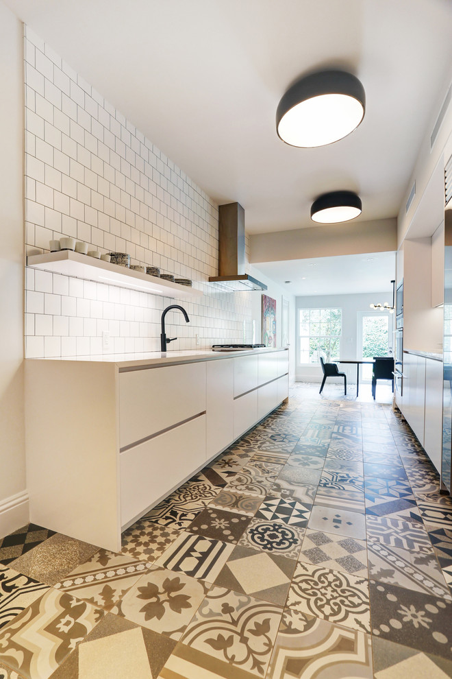 This is an example of a small bohemian galley enclosed kitchen in Miami with a submerged sink, flat-panel cabinets, white cabinets, composite countertops, white splashback, porcelain splashback, stainless steel appliances, porcelain flooring and no island.