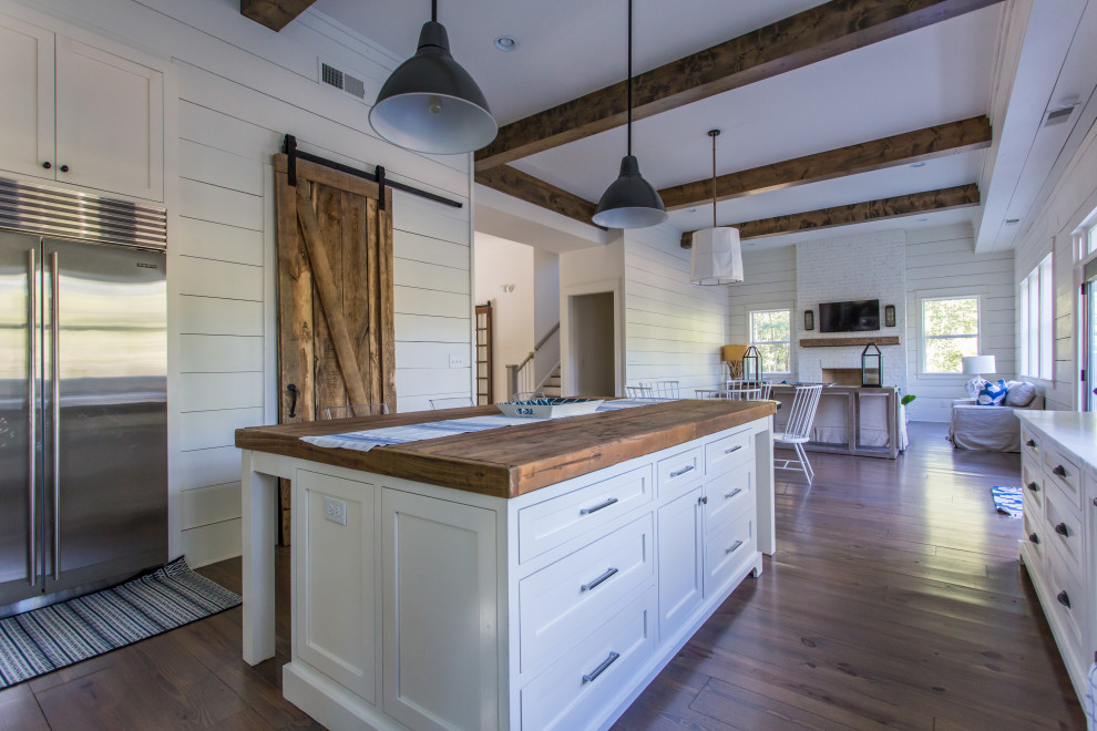 Inspiration for a rural l-shaped kitchen in Atlanta with a belfast sink, shaker cabinets, white cabinets, wood worktops, wood splashback, stainless steel appliances, dark hardwood flooring, an island, brown floors, brown worktops and exposed beams.