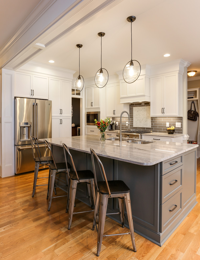 Inredning av ett klassiskt mellanstort grå grått kök, med en trippel diskho, luckor med infälld panel, vita skåp, granitbänkskiva, grått stänkskydd, stänkskydd i glaskakel, rostfria vitvaror, mellanmörkt trägolv, en köksö och brunt golv