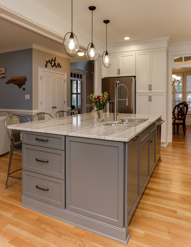 Medium sized classic l-shaped open plan kitchen in Raleigh with a triple-bowl sink, recessed-panel cabinets, white cabinets, granite worktops, grey splashback, glass tiled splashback, stainless steel appliances, medium hardwood flooring, an island, brown floors and grey worktops.