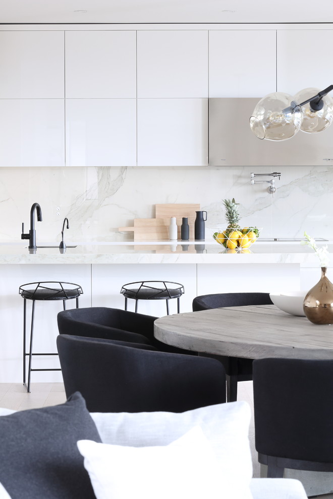Photo of a large modern l-shaped open plan kitchen in Vancouver with a submerged sink, flat-panel cabinets, white cabinets, marble worktops, white splashback, marble splashback, integrated appliances, medium hardwood flooring, an island, white floors and white worktops.