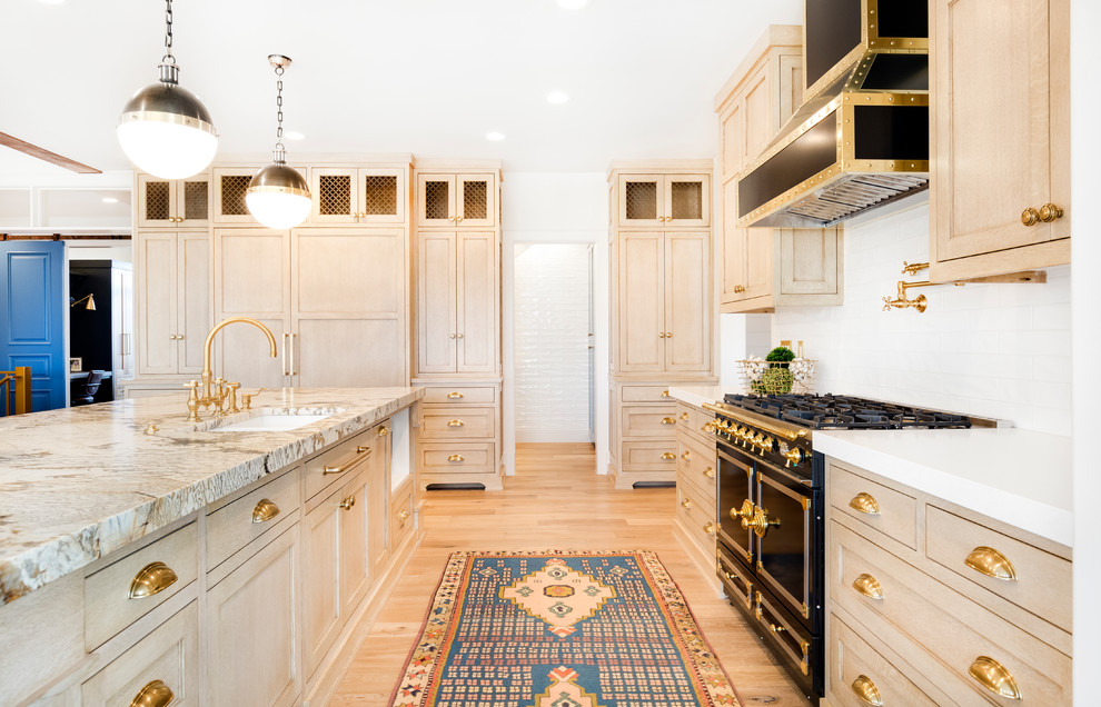 Eklektisk inredning av ett stort kök med öppen planlösning, med en nedsänkt diskho, skåp i ljust trä, marmorbänkskiva, vitt stänkskydd, svarta vitvaror och en köksö