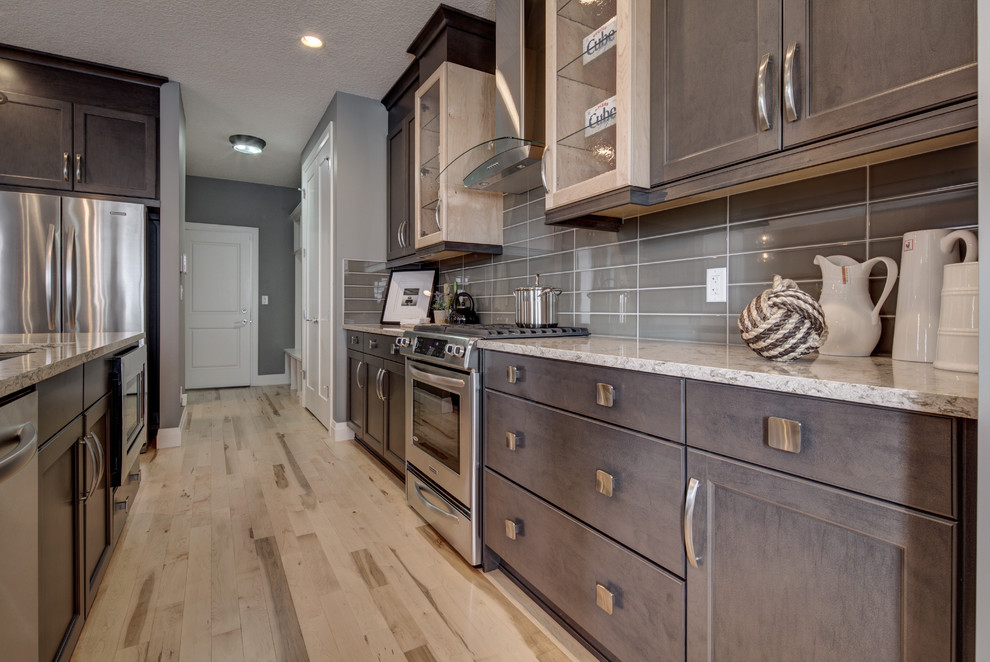 Example of a mid-sized eclectic l-shaped light wood floor and beige floor open concept kitchen design in Calgary with an undermount sink, recessed-panel cabinets, dark wood cabinets, quartz countertops, gray backsplash, glass tile backsplash, stainless steel appliances, an island and gray countertops