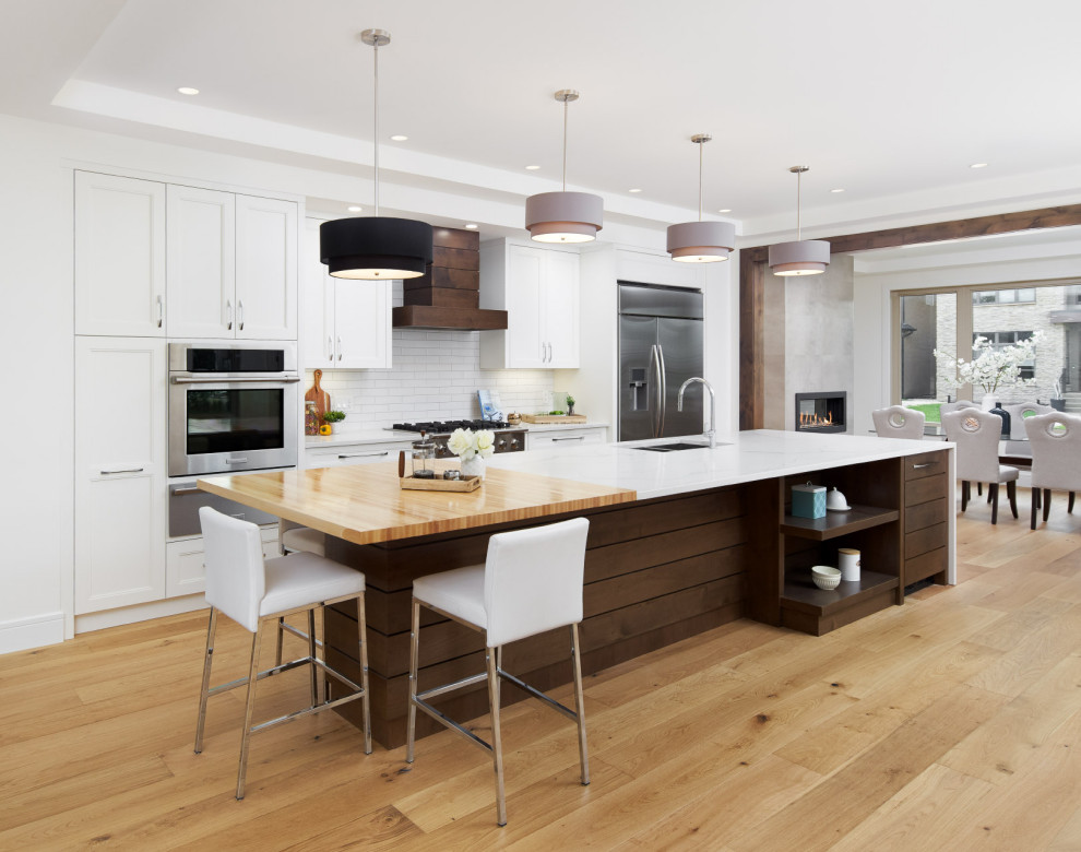 Inspiration for a mid-sized transitional galley light wood floor and brown floor kitchen remodel in Calgary with an undermount sink, shaker cabinets, white cabinets, quartz countertops, white backsplash, subway tile backsplash, stainless steel appliances, an island and white countertops