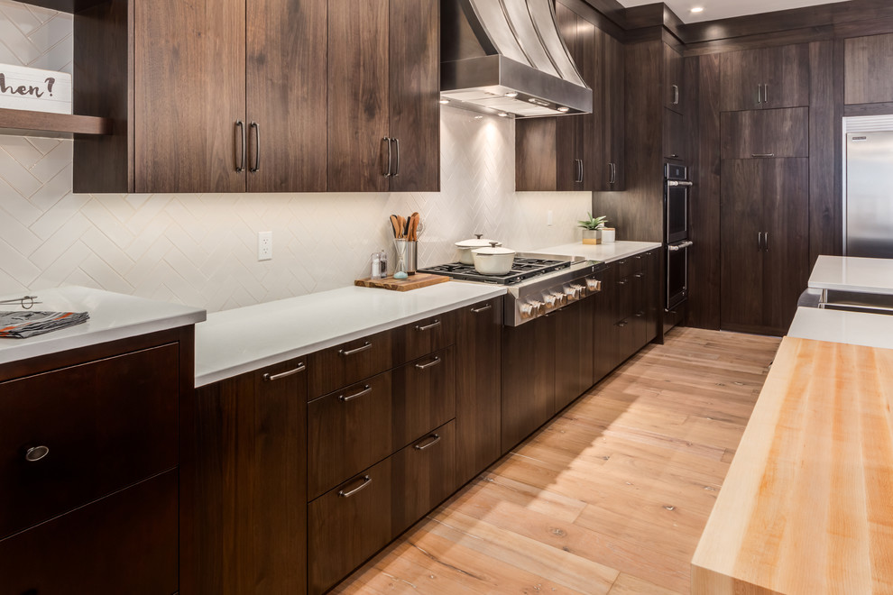 Example of a large country single-wall light wood floor and beige floor eat-in kitchen design in Calgary with a farmhouse sink, flat-panel cabinets, dark wood cabinets, quartz countertops, white backsplash, porcelain backsplash, stainless steel appliances and an island