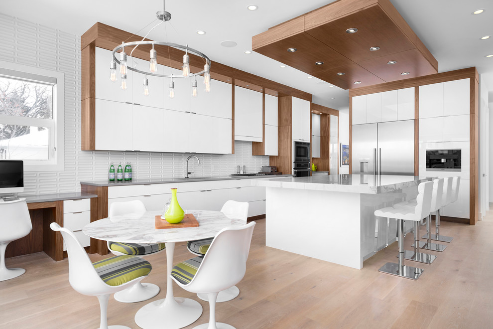 Large contemporary kitchen/diner in Calgary with white cabinets, granite worktops, white splashback, stainless steel appliances, light hardwood flooring, an island, flat-panel cabinets, beige floors and grey worktops.