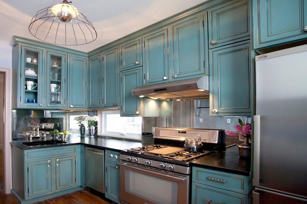 This is an example of a classic l-shaped enclosed kitchen in New York with stainless steel appliances, blue cabinets, soapstone worktops, mirror splashback and beaded cabinets.