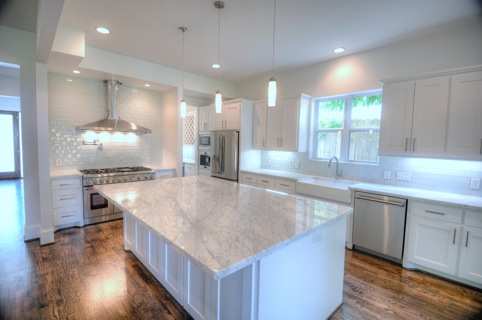 Example of a large trendy galley dark wood floor eat-in kitchen design in Houston with a farmhouse sink, shaker cabinets, white cabinets, marble countertops, blue backsplash, glass tile backsplash, stainless steel appliances and an island